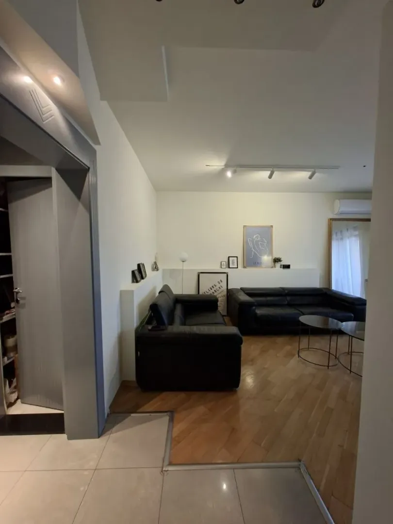Living room with black leather sofas and wooden flooring.