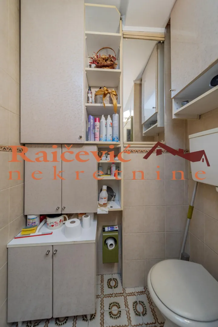 Manje kupatilo sa ugradnim ormarićima, WC šoljom i ogledalom.