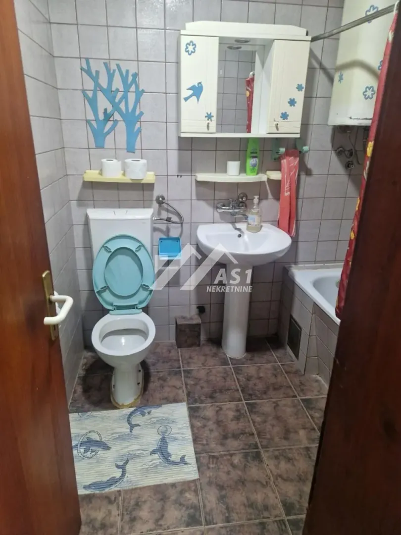 Manje kupatilo sa wc šoljom, umivaonikom i kadom obloženo pločicama.