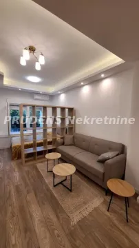 Living room with a sofa, coffee tables, and a partition shelving unit. - image 12