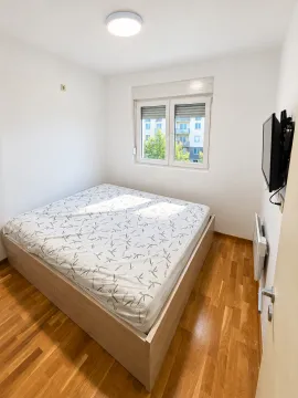 Manja spavaća soba sa bračnim krevetom, drvenim podom i televizorom na zidu. - image 6