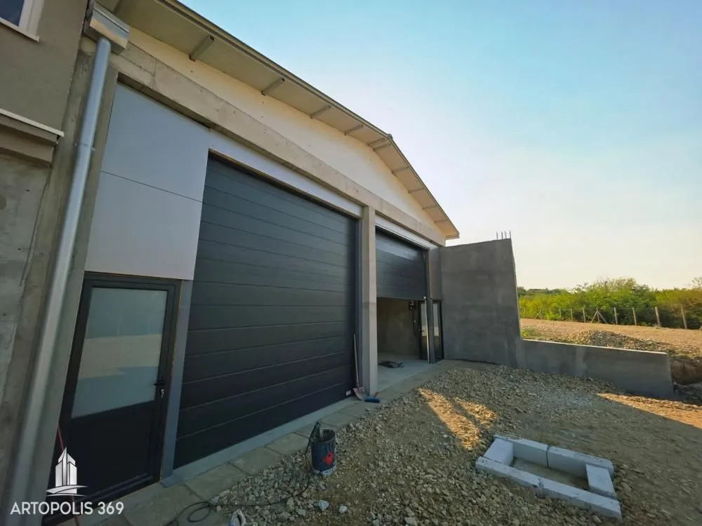 Exterior view of the building with garage doors and driveway under construction.