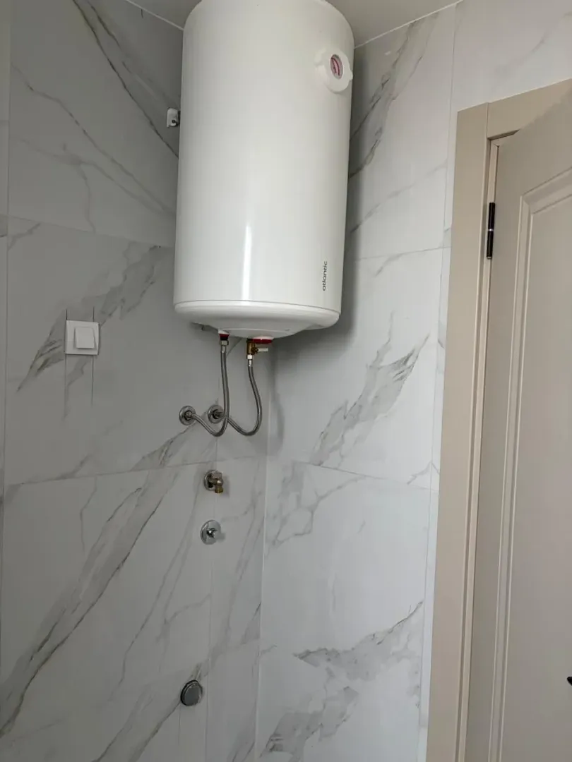 Bathroom with a mounted water heater and marble tiles.