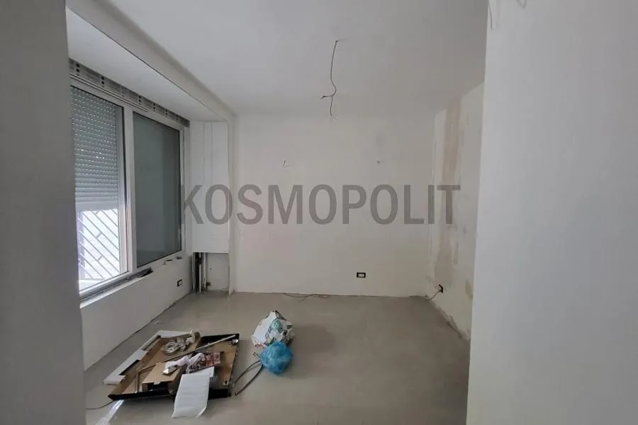 Prazna neuređena prostorija sa velikim prozorom i građevinskim materijalom na podu.