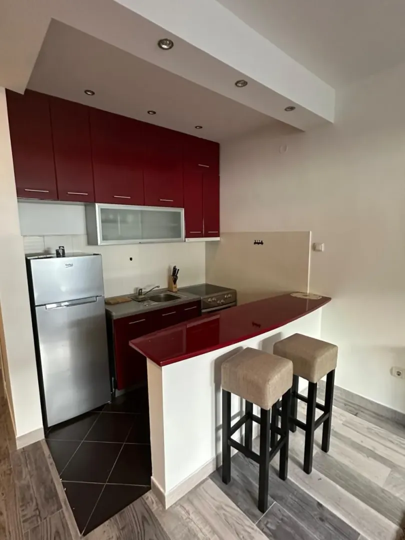 Small kitchen with red cabinets, a breakfast bar, and two bar stools.