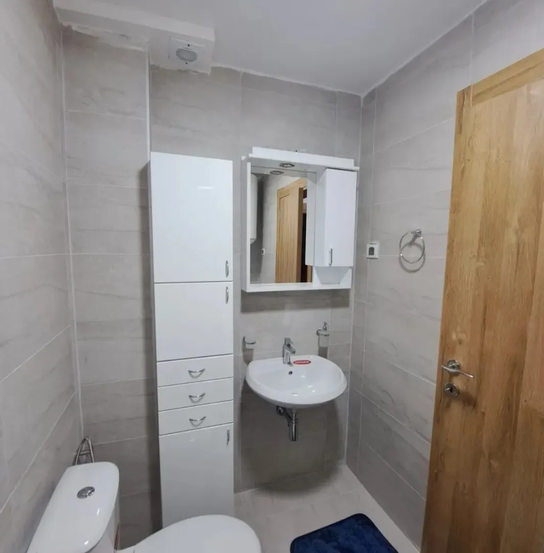 Manje kupatilo obloženo keramičkim pločicama sa umivaonikom, ogledalom i WC šoljom.