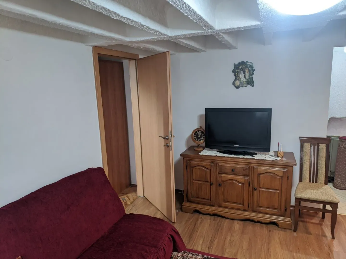 Living room featuring a wooden cabinet, television, and a red sofa.