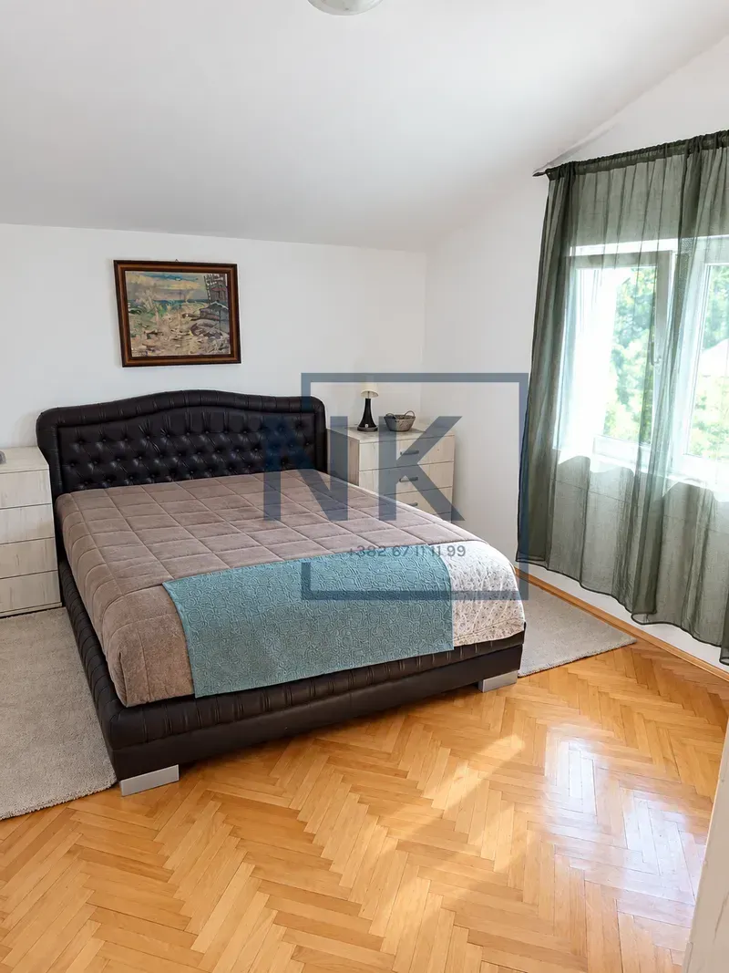 Bedroom with a large bed with a leather headboard, parquet flooring, and a window with curtains.