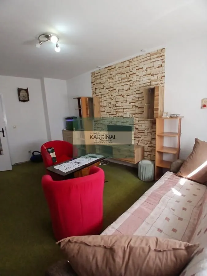 Dnevna soba sa garniturom, crvenim foteljama i ukrasnim zidom.