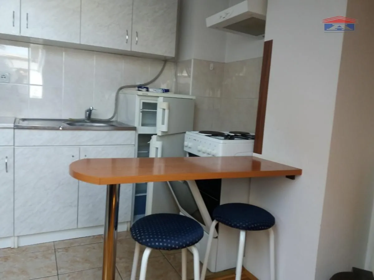 Manja kuhinja sa elementima, frižiderom, šporetom i šankom sa dve stolice.