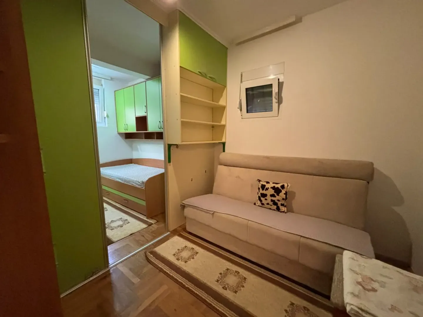 Manja dnevna soba sa kaučem i prolazom u spavaću sobu sa zelenim elementima.
