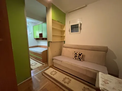 Manja dnevna soba sa kaučem i prolazom u spavaću sobu sa zelenim elementima. - image 9