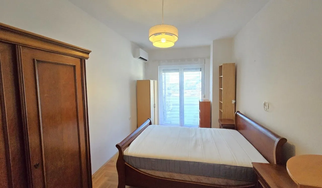 Spavaća soba sa bračnim krevetom, drvenim ormarom i balkonskim vratima.