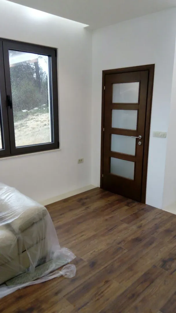 Soba sa laminatom, velikim prozorom i drvenim vratima sa staklenim detaljima.