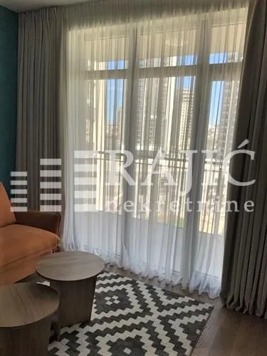 Living room with a sofa, coffee tables and a large window with curtains.