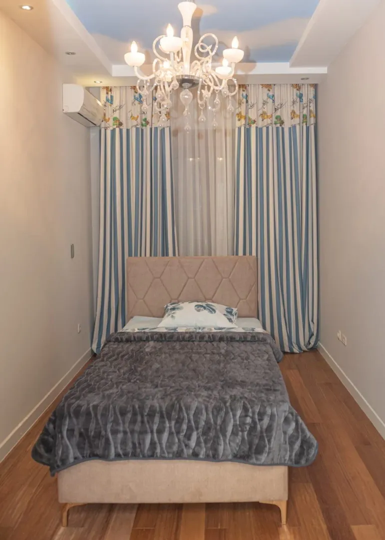 Children's bedroom with a bed, chandelier, and blue-and-white curtains.