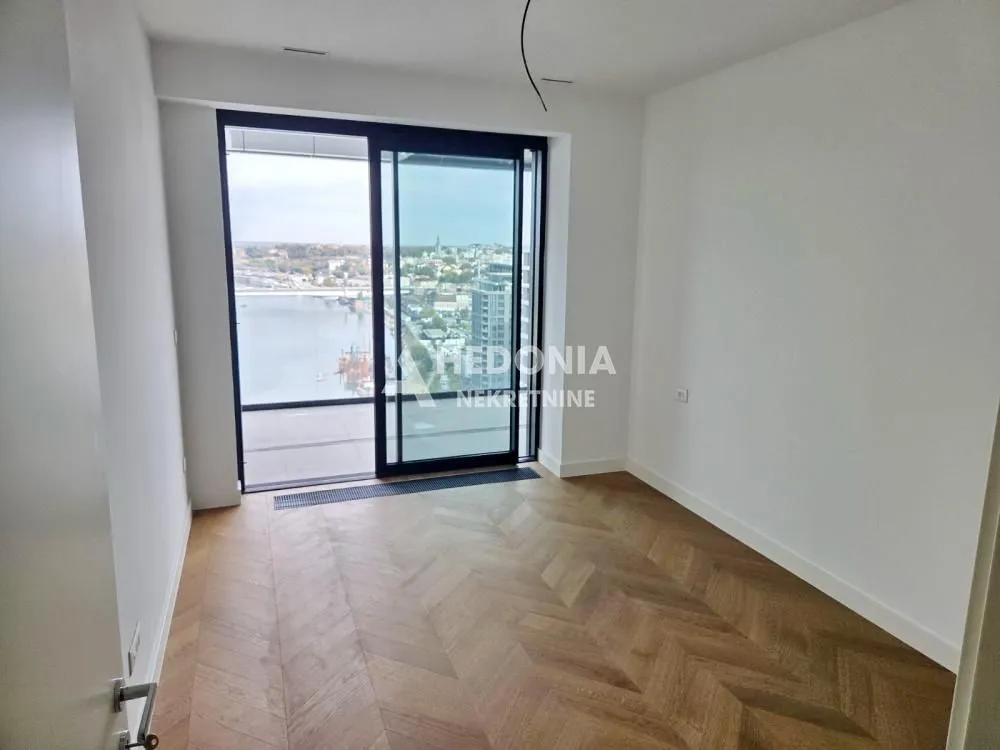 Empty room with hardwood parquet flooring and access to a terrace with a river view.