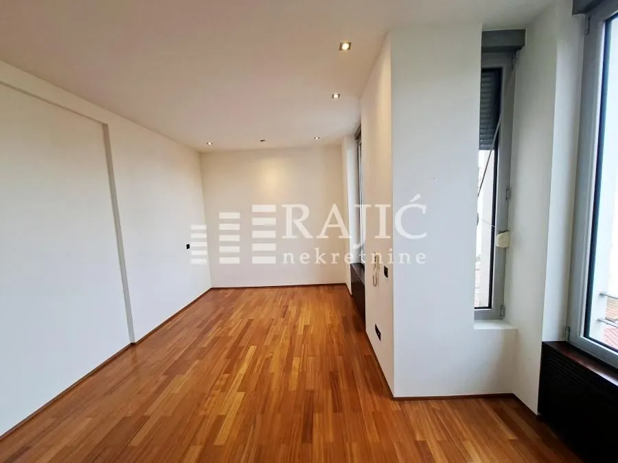 Empty room with parquet flooring and large windows.