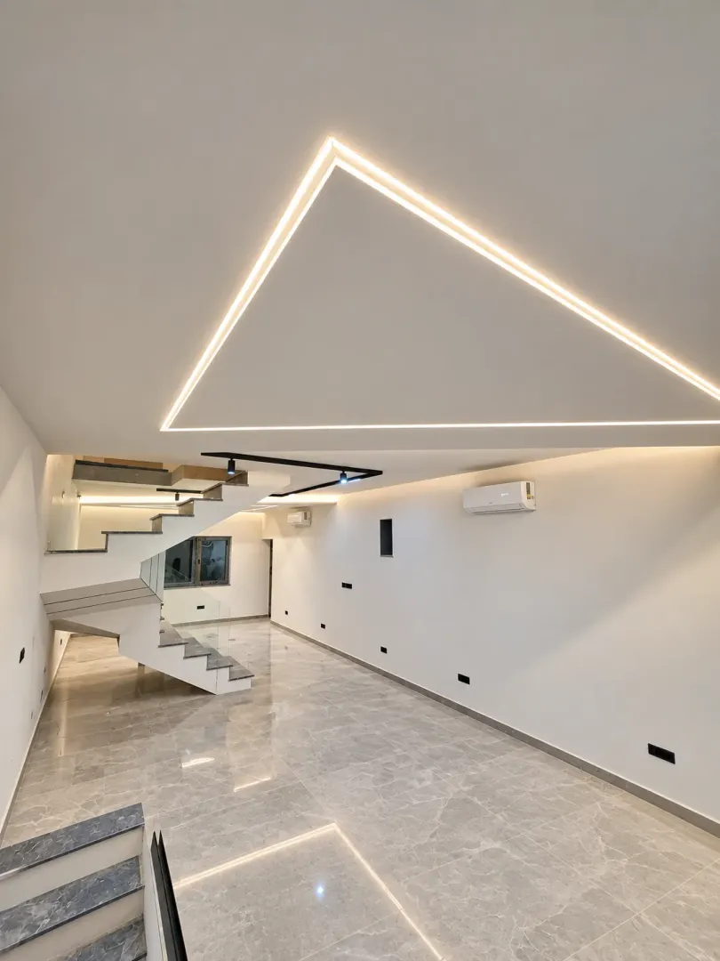 Modern empty living room with a staircase and built-in ceiling lighting.