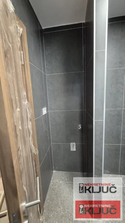 Pogled na kupatilo sa tamnim pločicama i ugrađenim sanitarnim instalacijama.