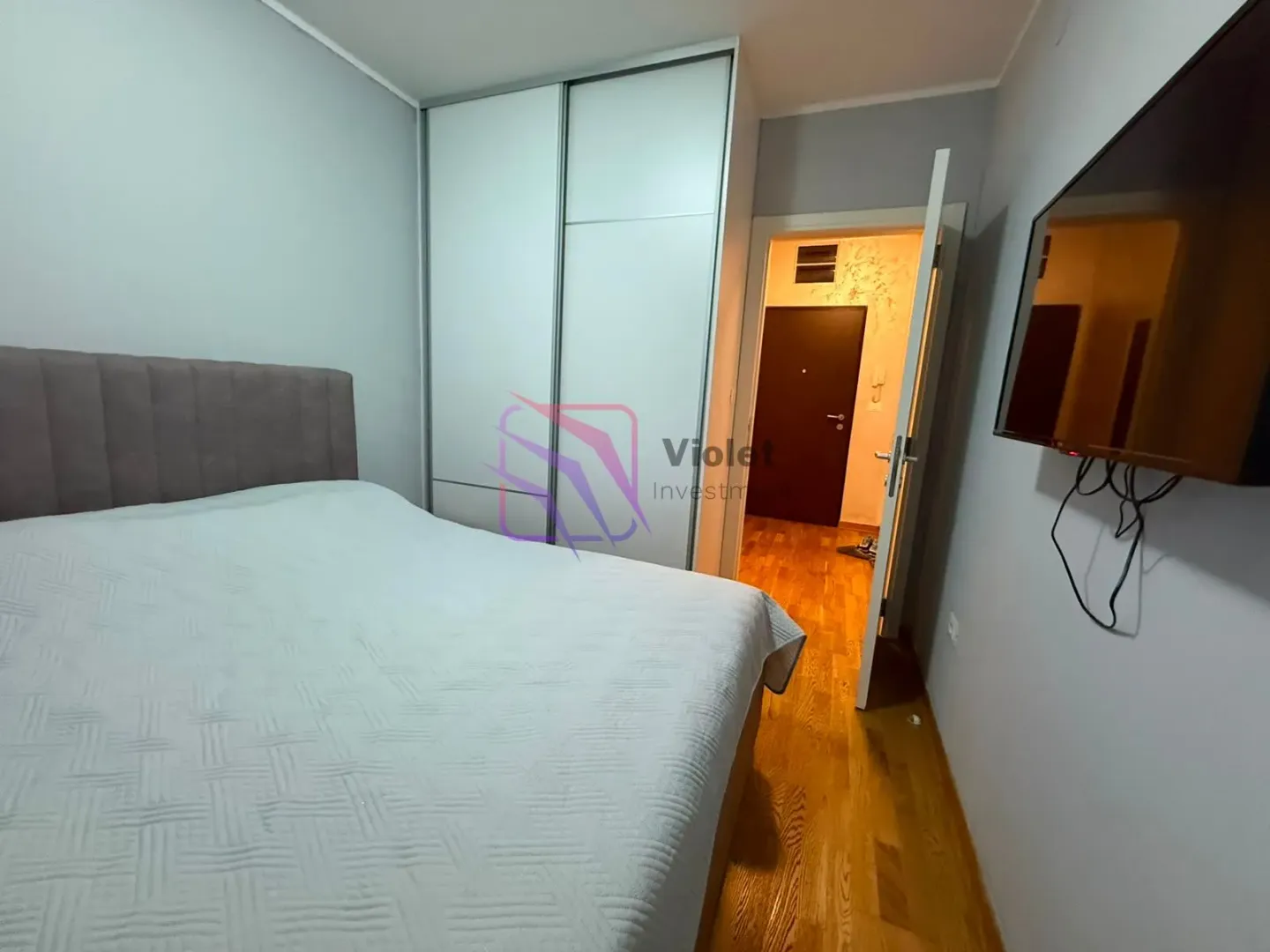 Furnished bedroom with a double bed, wardrobe, and wall-mounted TV.