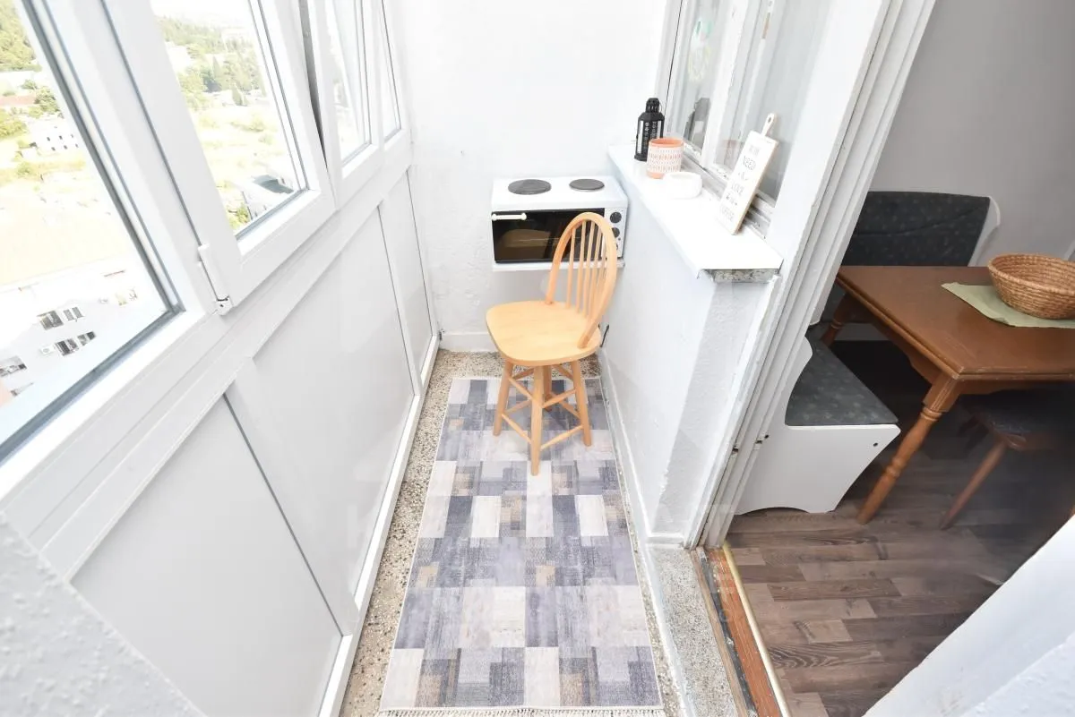 Zastakljeni balkon sa malom stolicom i trpezarijskim stolom.