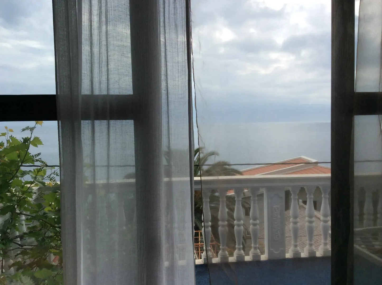 Pogled na more sa terase kroz prozor sa zavjesama.