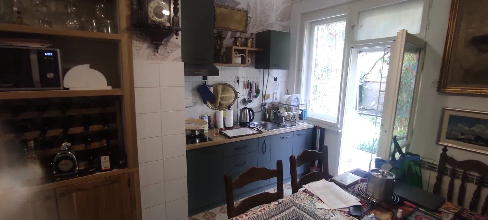 Kuhinja sa tamnim elementima i trpezarijskim stolom u prvom planu.