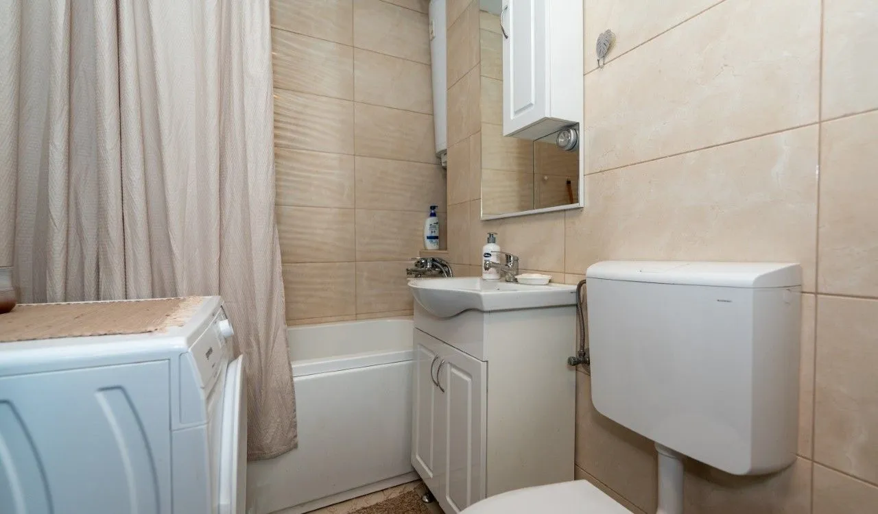 Small bathroom with a bathtub, washbasin, toilet, and washing machine.