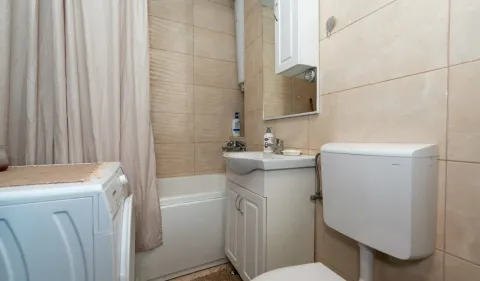 Small bathroom with a bathtub, washbasin, toilet, and washing machine. - image 9