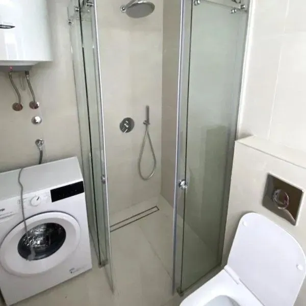 Smaller bathroom with a shower cabin, toilet, and washing machine.