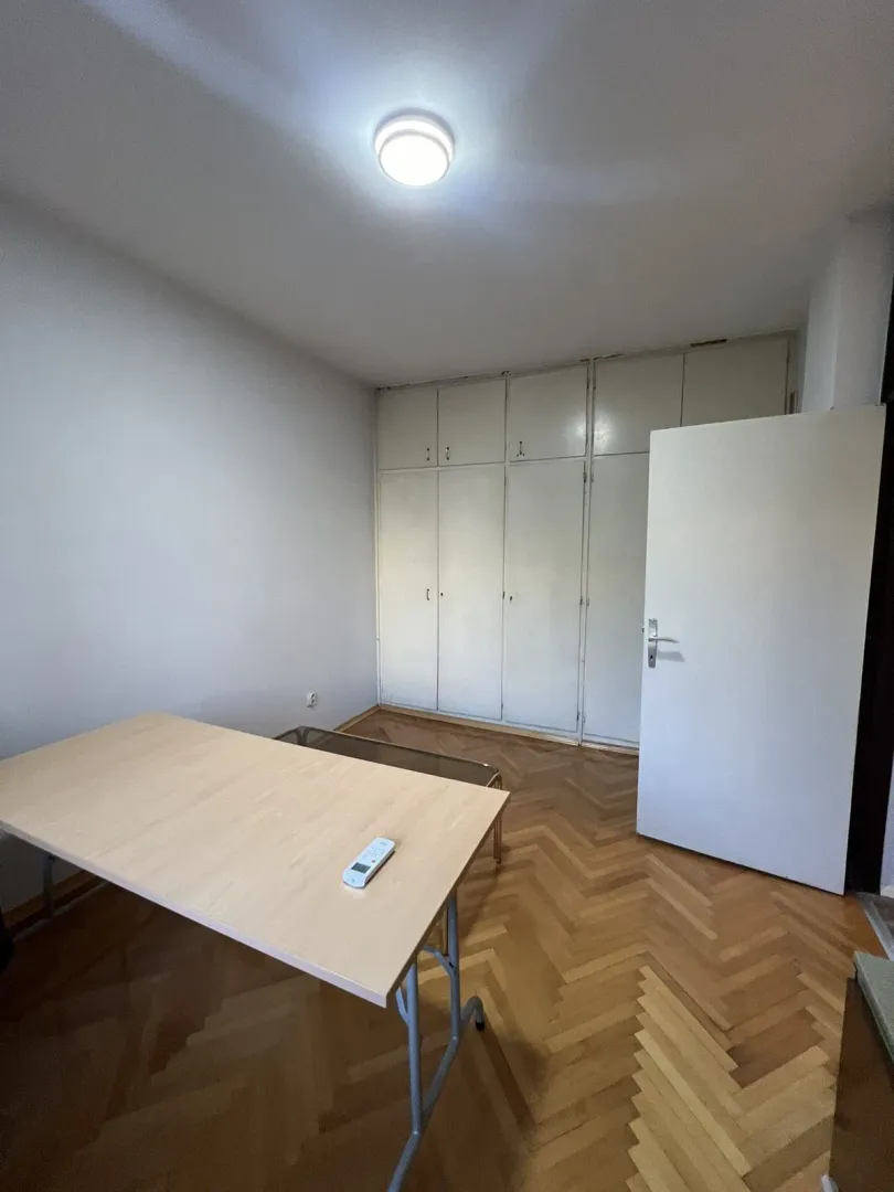 A bright and simple room featuring a built-in wardrobe, a table, and parquet flooring.