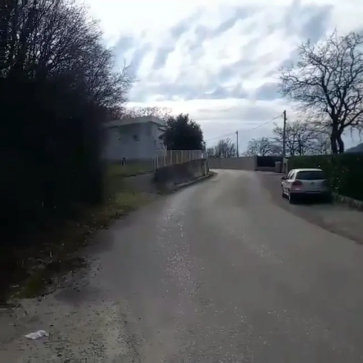 Asfaltni put koji vodi prema naselju sa kućama i zelenilom.