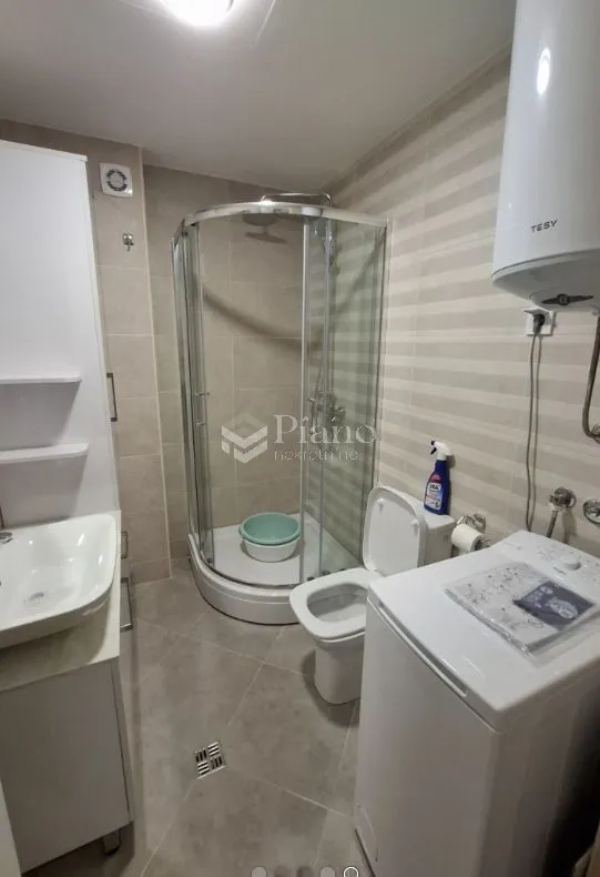 Bathroom with a shower cabin, sink, toilet, and washing machine.