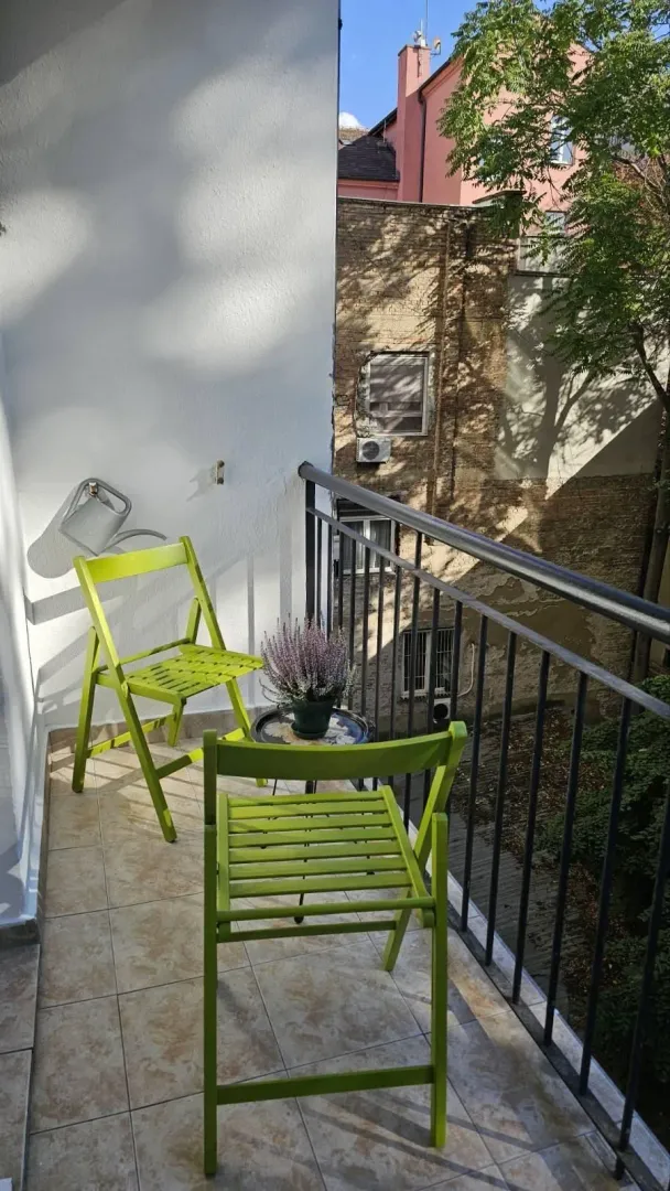 Small furnished balcony with metal railing and view of neighboring buildings.