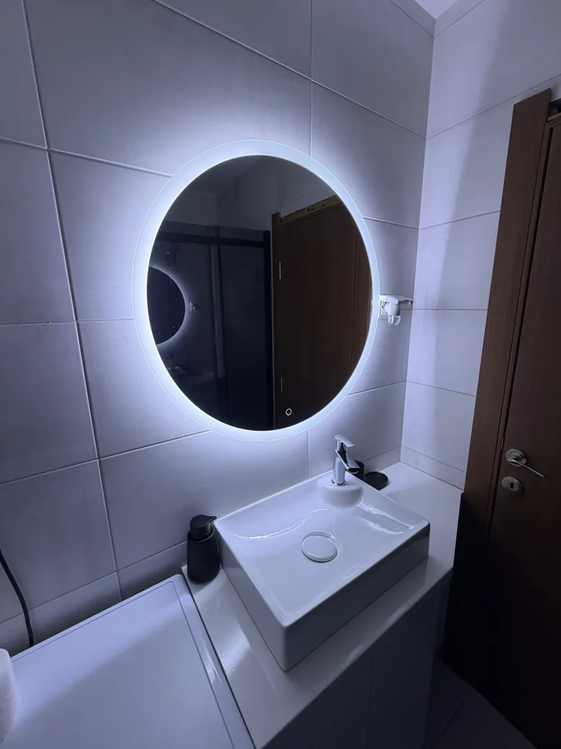 Modern bathroom with a washbasin and a round backlit mirror.