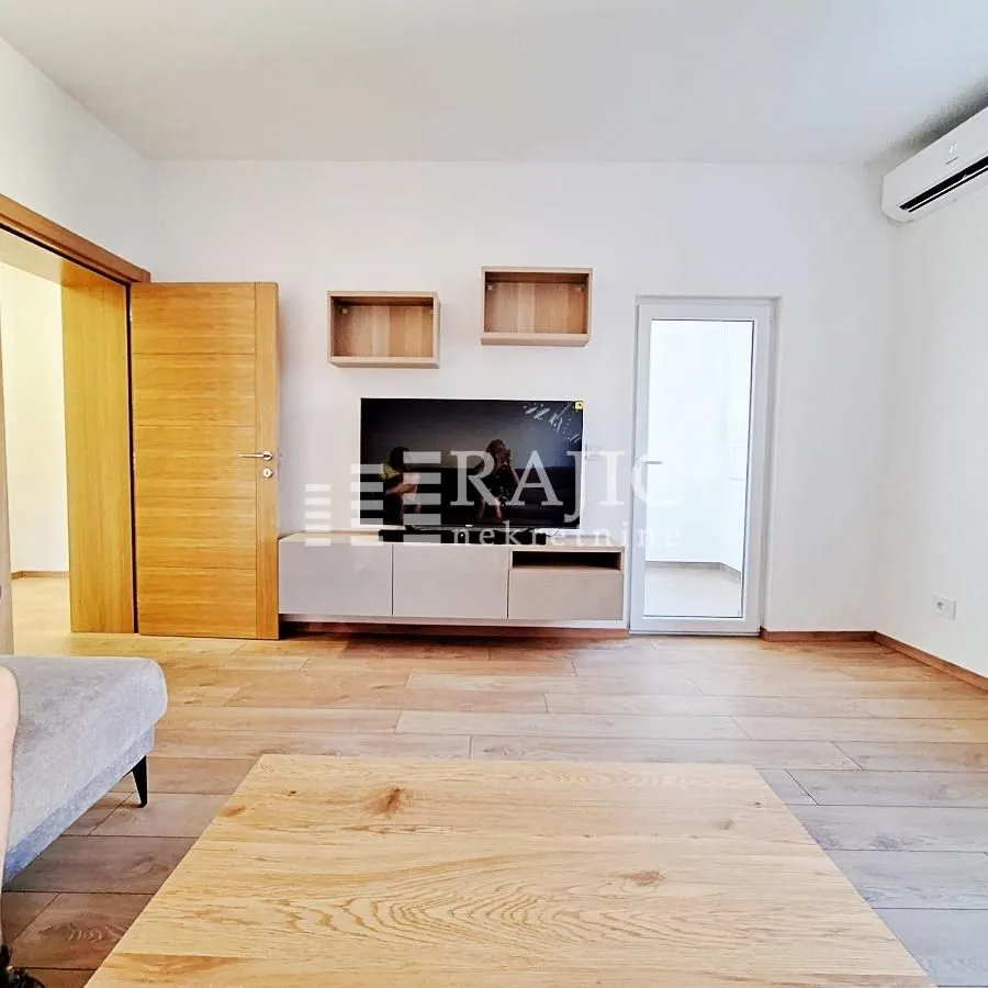 Living room with wooden flooring, TV unit, and access to the terrace.