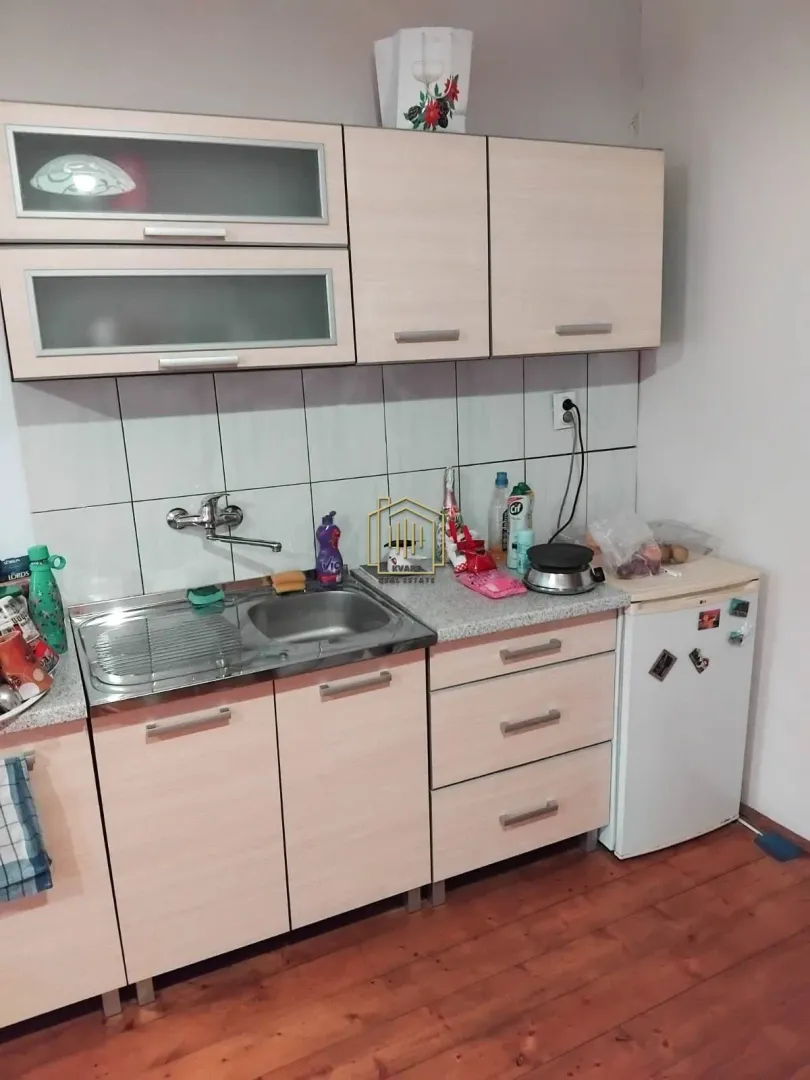Manja kuhinja sa drvenim elementima, sudoperom i malim frižiderom.