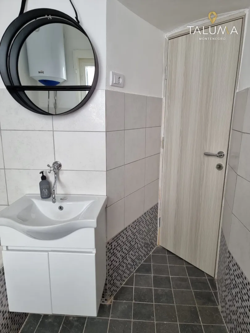 Smaller bathroom with a washbasin, round mirror, and a door.