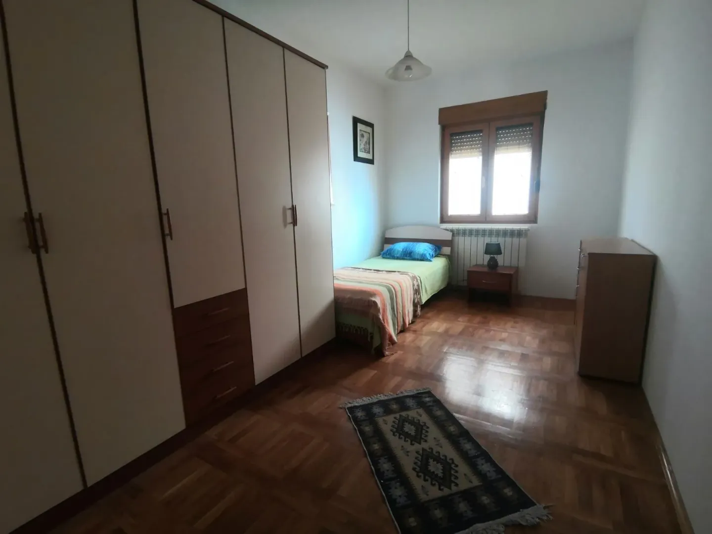 Jednostavna spavaća soba sa jednim krevetom i velikim ormarom.
