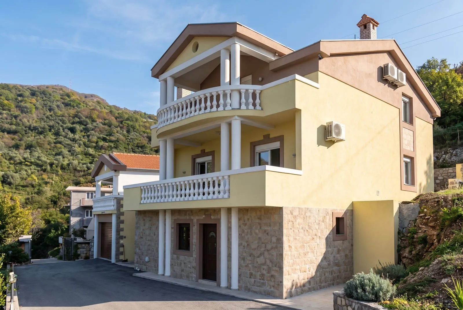 Vanjski izgled trospratne kuće sa kamenom fasadom i balkonima.