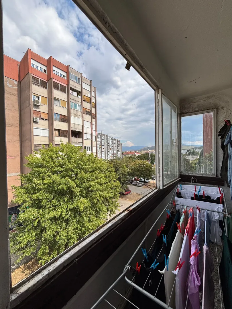 Zastakljeni balkon sa sušilicom za veš i pogledom na naselje.