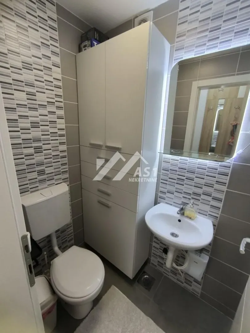 Smaller bathroom with a toilet, washbasin, mirror and a white cabinet.