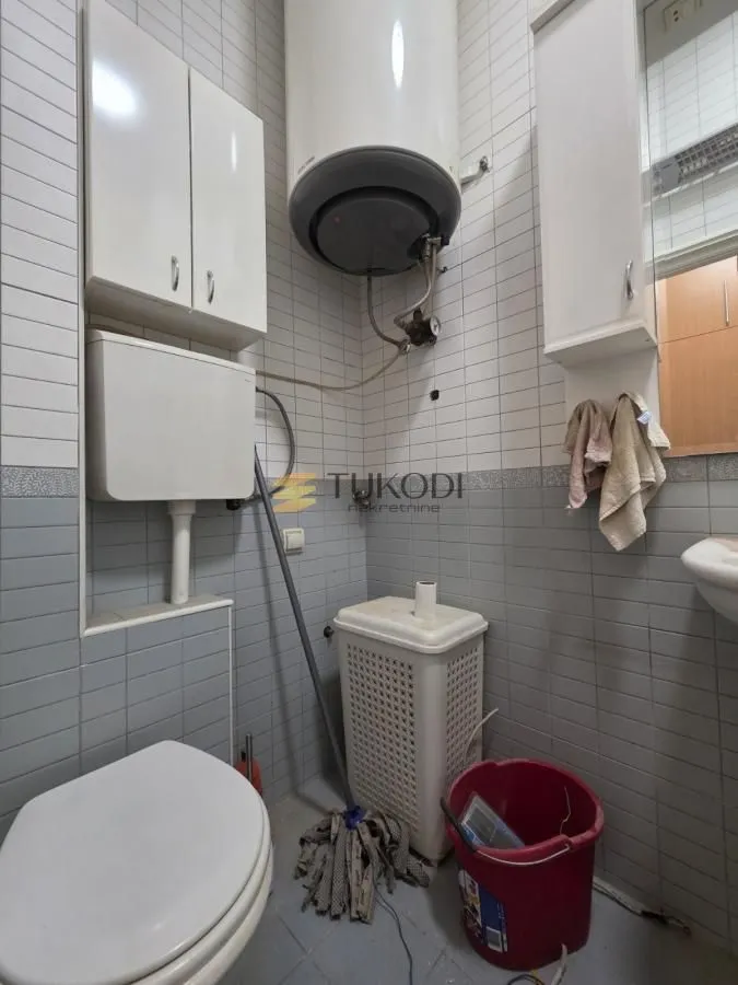 Smaller bathroom with tiles, toilet, water heater and wall cabinets.