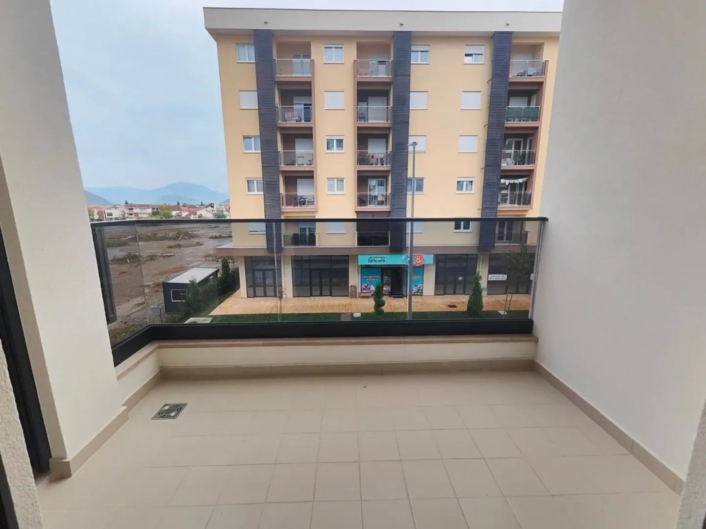 Spacious unfurnished balcony with a glass railing and a view of surrounding buildings.