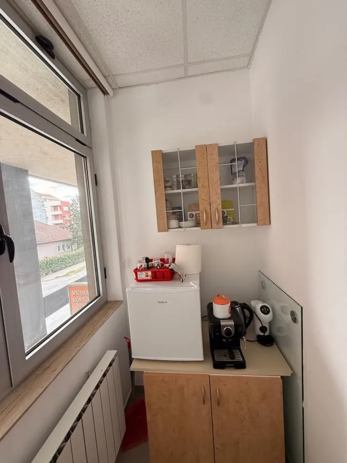 Small kitchenette with cabinets and a refrigerator next to the window.