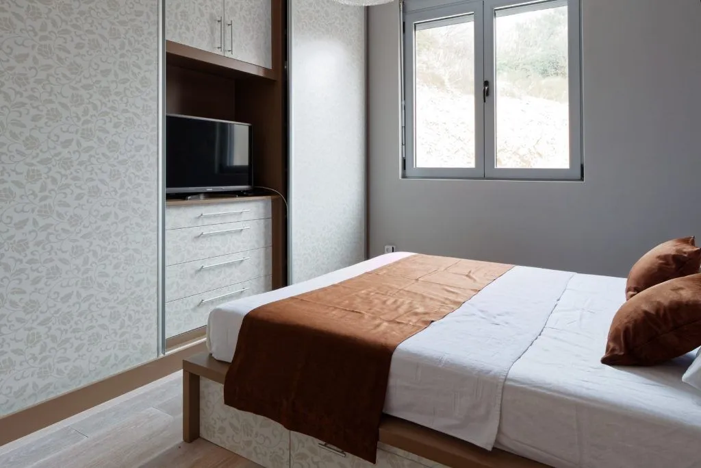 Furnished bedroom with a double bed and a built-in wardrobe with a television.