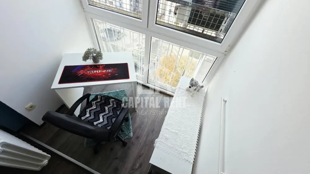 Glazed balcony furnished with a desk and chair next to a large window.
