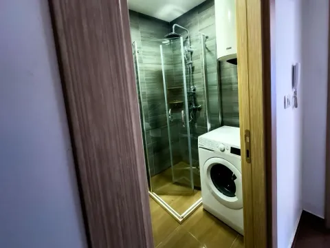 Pogled kroz otvorena vrata na kupatilo sa tuš kabinom i veš mašinom. - image 4