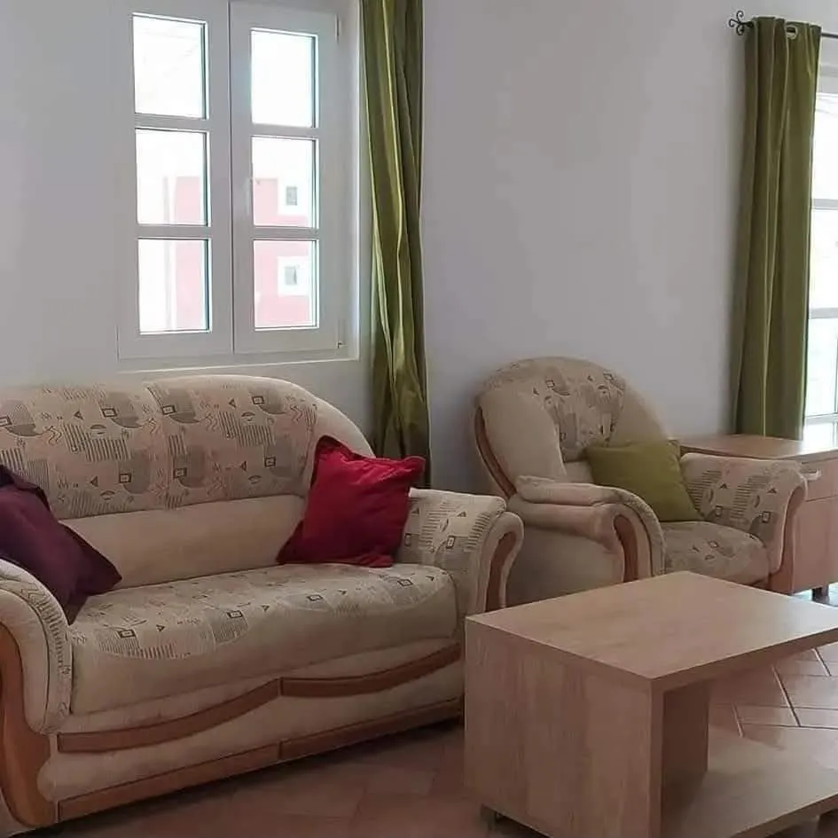 Living room with a sofa set, armchair, coffee table, and a window with green curtains.